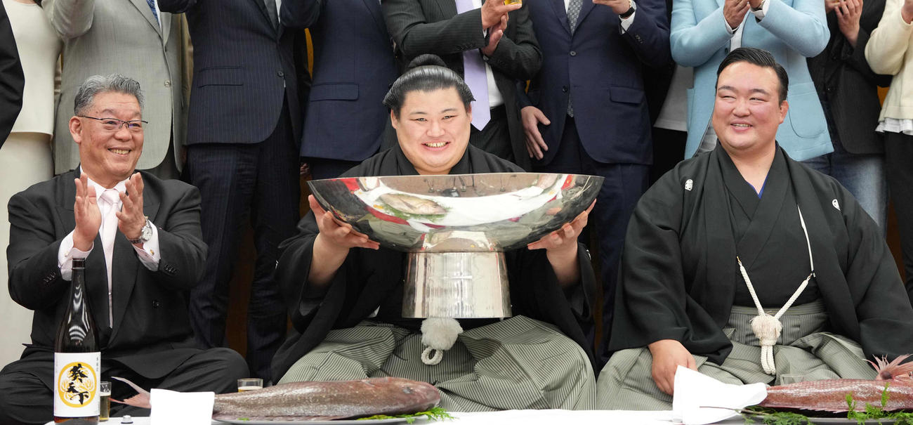 お祝いのお酒が注がれた銀杯を持ち上げる大の里。左は二所ノ関部屋大東後援会の橋本正幸会長、右は二所ノ関親方（撮影・小沢裕）