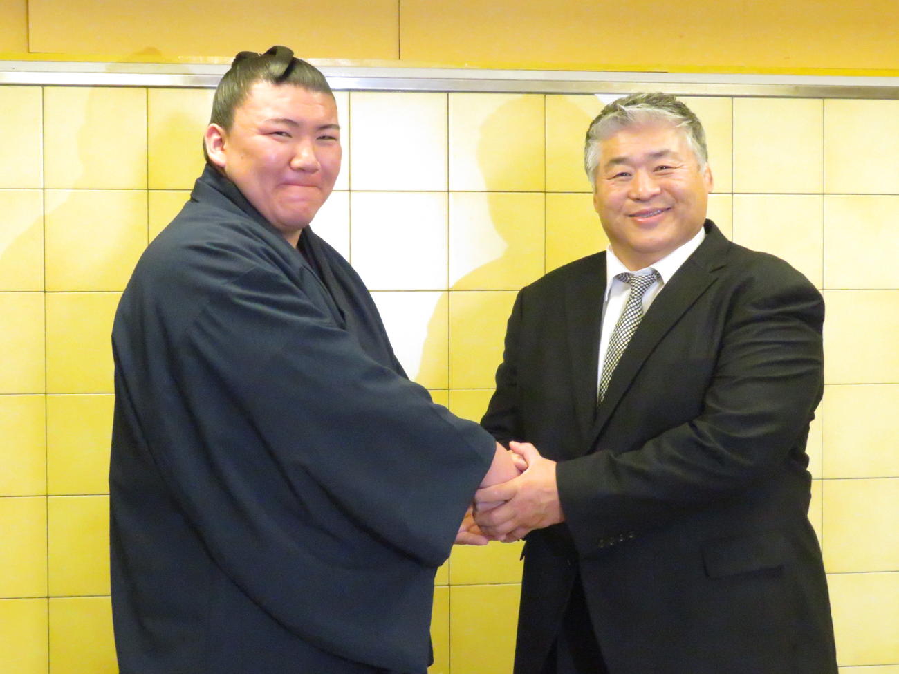 新十両会見で師匠の大嶽親方（右）と握手を交わす夢道鵬