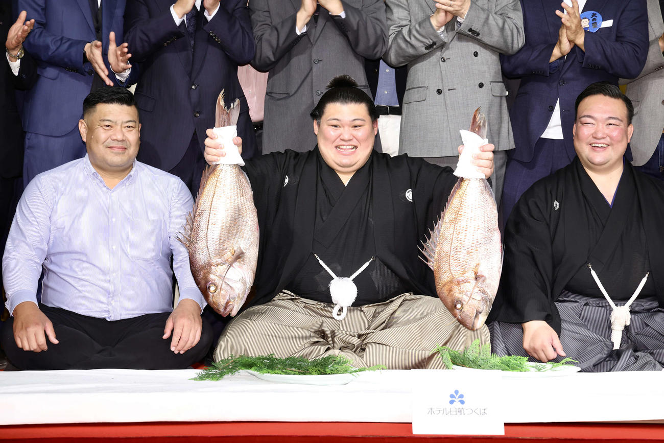 鯛持ちで笑顔を見せる大の里（中央）。左は父・中村知幸さん、右は二所ノ関親方（撮影・河田真司）