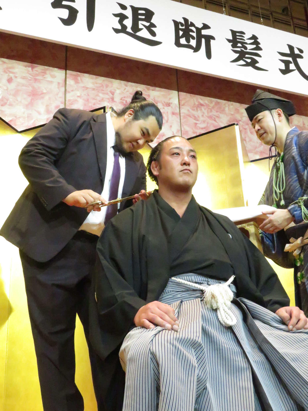 元旭大星（中央）の断髪式でハサミを入れた、元北青鵬のダワーニンジ氏（左）