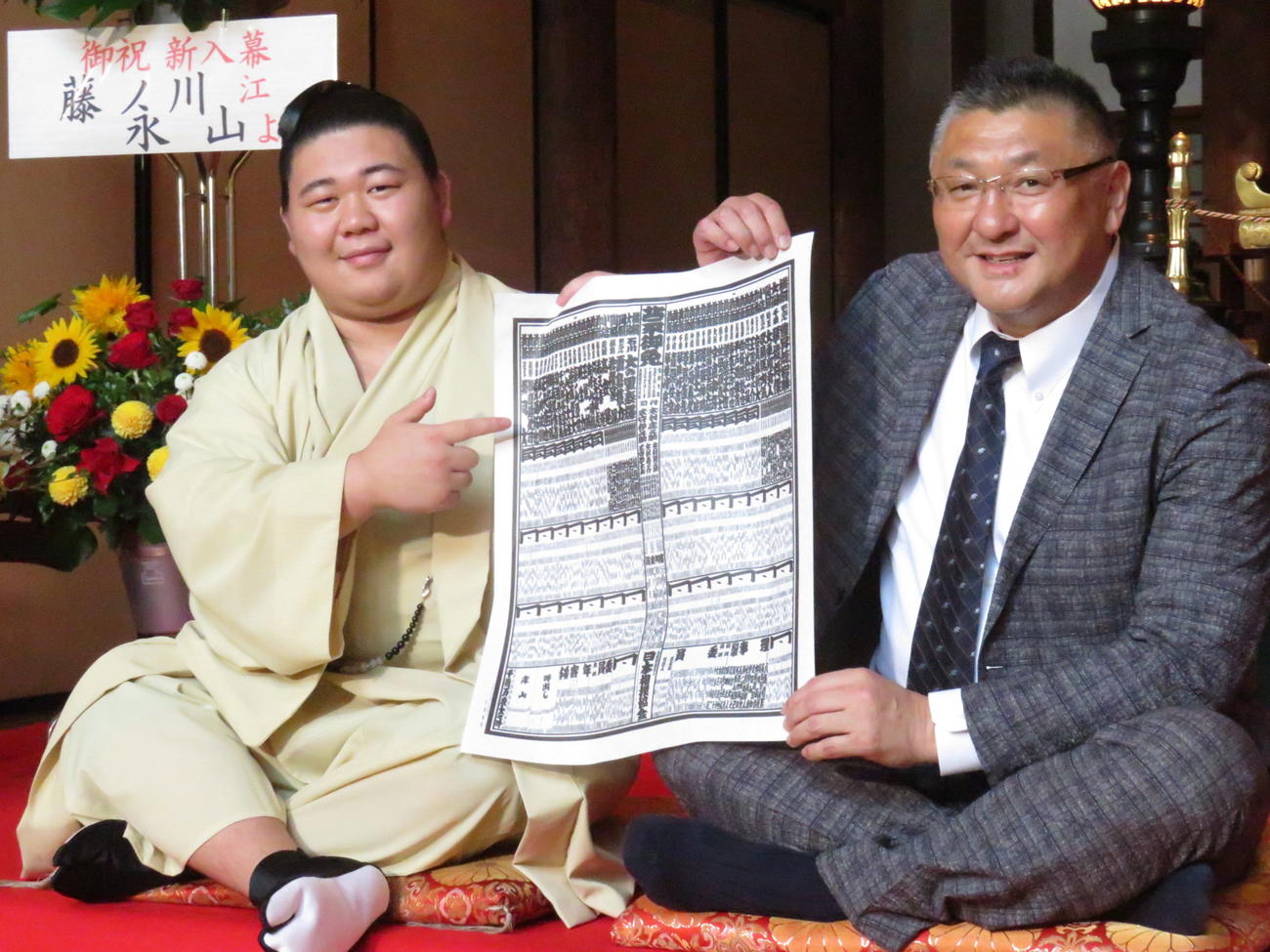 師匠の伊勢ノ海親方（右）とともに新入幕会見に臨んだ若碇改め藤ノ川は、新番付の自身のしこ名を指さして笑顔を見せた