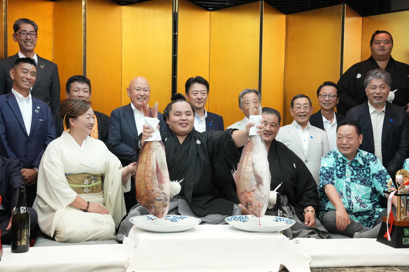 関係者の祝福を受けながら両手でお祝いのタイを掲げる琴勝峰（撮影・小沢裕）