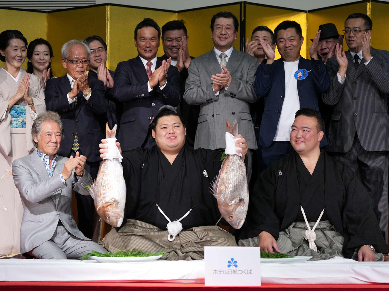 千秋楽パーティーで関係者の祝福を受けながらお祝いのタイを持つ大の里。右は師匠の二所ノ関親方（撮影・小沢裕）