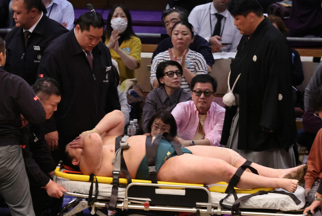 十両の三田（右）は輝に浴びせ倒しで敗れ土俵に座り込んだがしばらくして寝転び、担架からストレッチャーに移され退場（撮影・西尾就之）