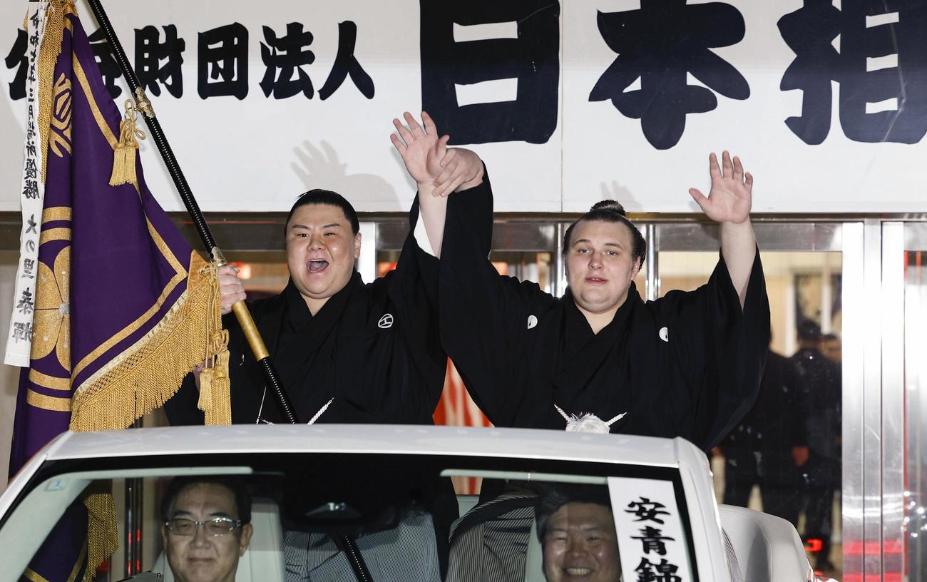 大相撲九州場所で初優勝を果たし、パレードで手を振る安青錦。左は義ノ富士＝23日、福岡市の福岡国際センター（共同）