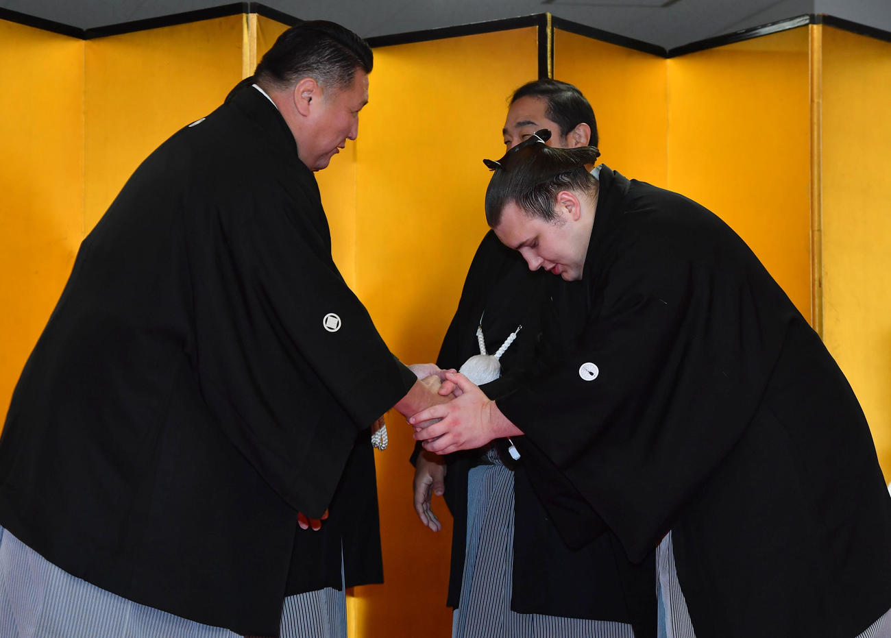 大関昇進の伝達式を終え、使者を務めた大島親方（左、元関脇旭天鵬）と握手を交わす安青錦（撮影・岩下翔太）