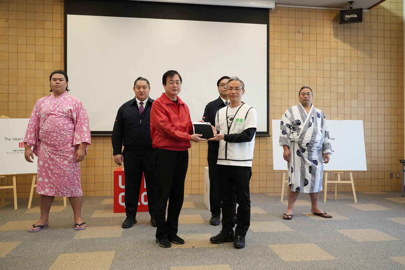 三道山子ども食堂事務局の田中策次郎氏（前列左）にヒートテックを手渡すファーストリテイリングの清智彦グループ執行役員。後列は左から、可貴、北陣親方、竹縄親方、栃登