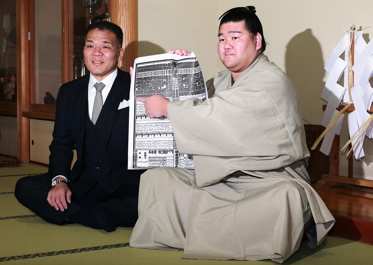 初場所での新入幕を決め、番付表を手にする羽出山。左は玉ノ井親方（撮影・野上伸悟）