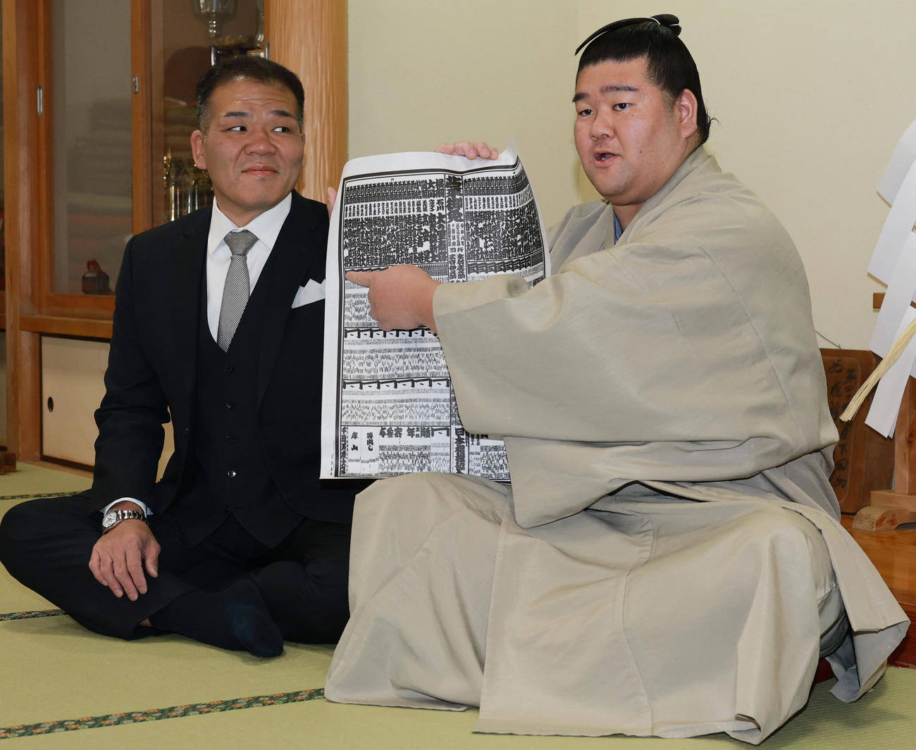初場所での新入幕を決め、番付表を手にする羽出山。左は玉ノ井親方（撮影・野上伸悟）