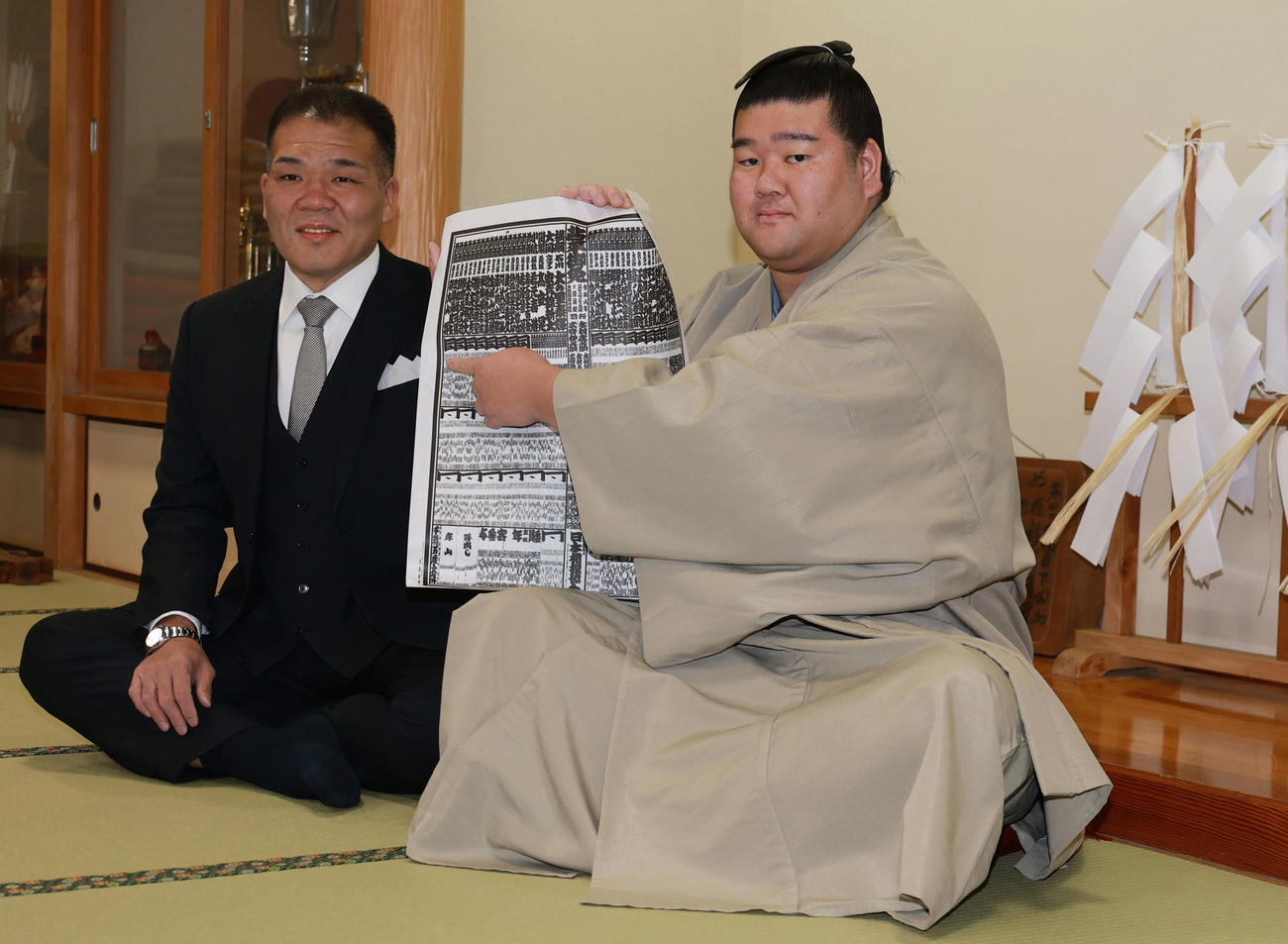 初場所での新入幕を決め、番付表を手にする羽出山。左は玉ノ井親方（撮影・野上伸悟）