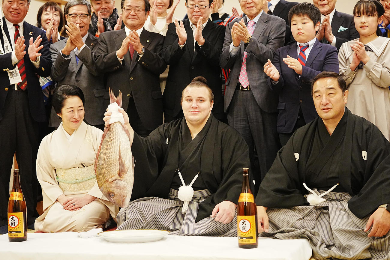 関係者の祝福を受けながらお祝いの鯛を持ち上げる安青錦。右は師匠の安治川親方、左はおかみの絵莉さん（撮影・小沢裕）