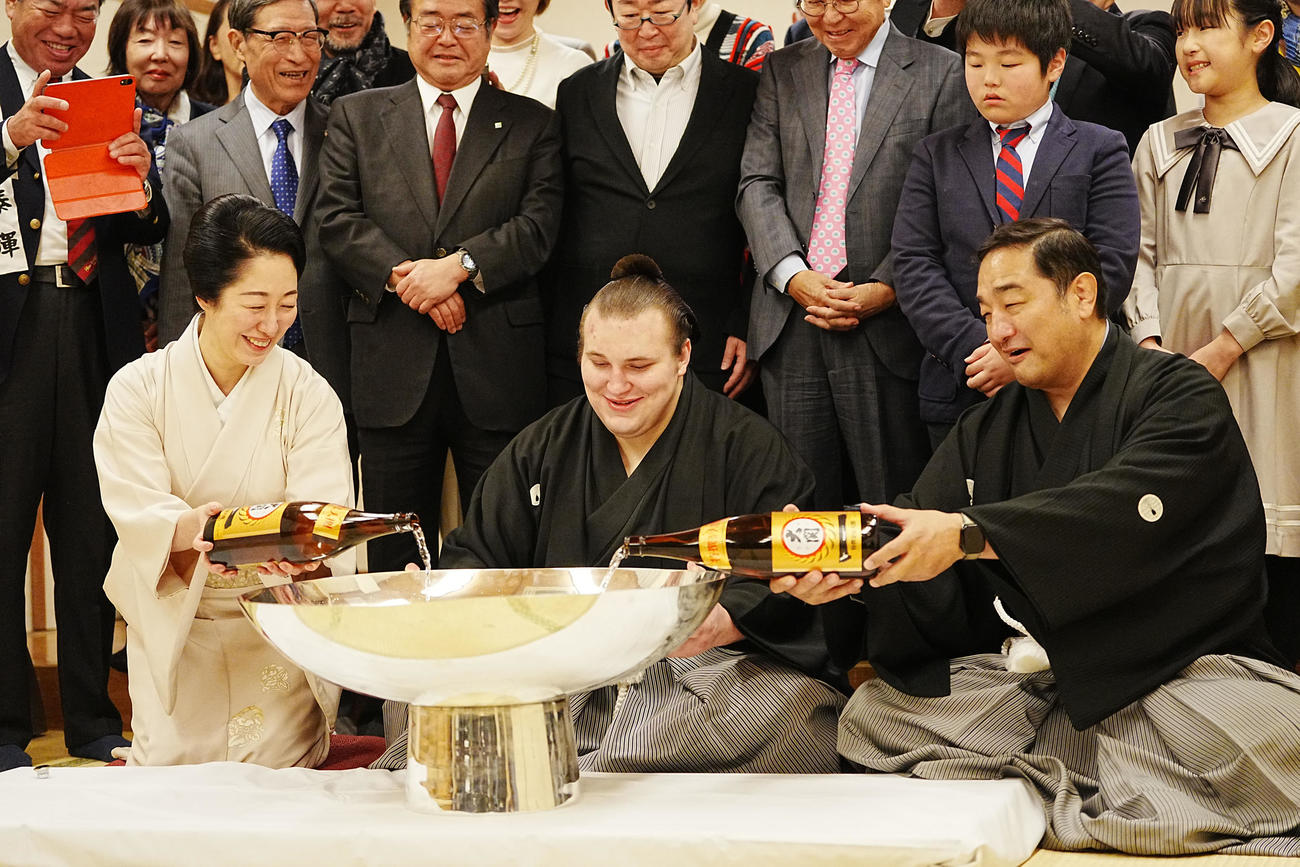 関係者の祝福を受けながら師匠の安治川親方（右）、おかみの絵莉さん（左）から銀杯にお酒を注いでもらう安青錦（撮影・小沢裕）