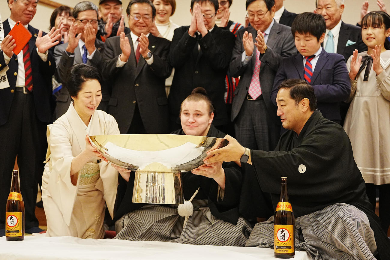 関係者の祝福を受けながら師匠の安治川親方（右）、おかみの絵莉さん（左）から銀杯に注いでもらったお酒を飲む安青錦（撮影・小沢裕）