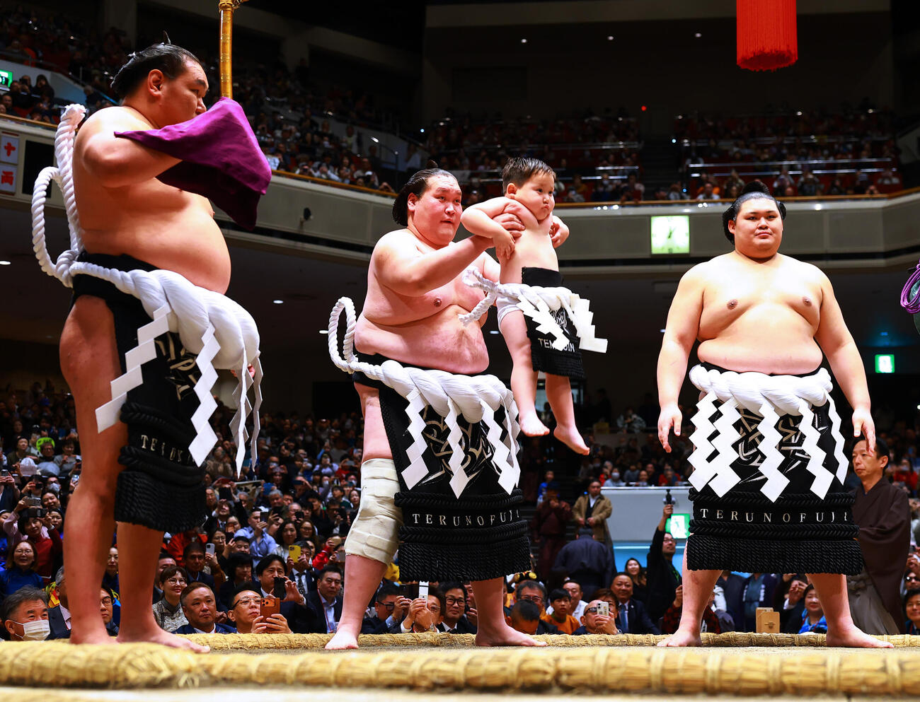 土俵入りで長男テムジン君を抱え上げる元照ノ富士の伊勢ケ浜親方。左は太刀持ちの豊昇龍、右は露払いの大の里（撮影・野上伸悟）