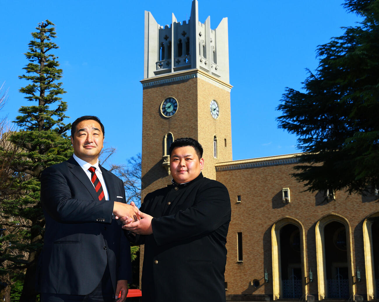 安治川部屋入門が決まり、早大大隈講堂を背に安治川親方（左）と握手する早大・川副（撮影・野上伸悟）