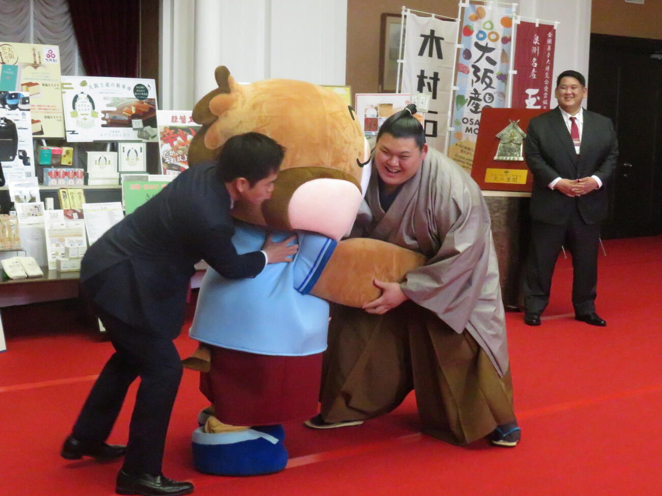 大の里（右）は要請を受け、大阪府の公式キャラクター、もずやん（中央）と相撲を取っていると、大阪府の吉村知事が加勢してきた。右後方は阿武松親方