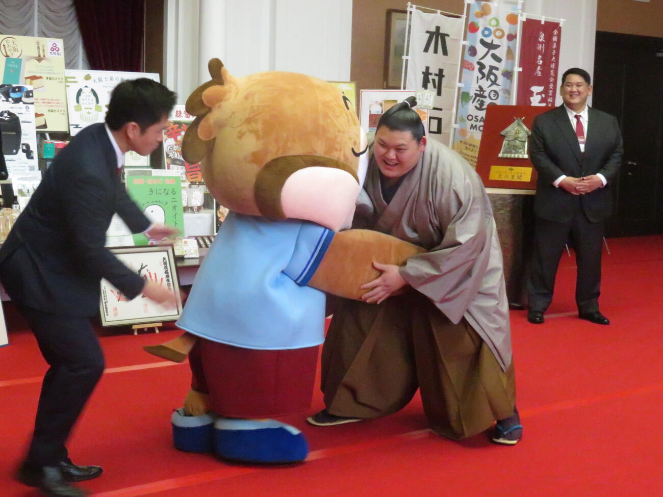 大の里（右）は要請を受け、大阪府の公式キャラクター、もずやん（中央）と相撲を取っていると、大阪府の吉村知事が加勢してきた。右後方は阿武松親方