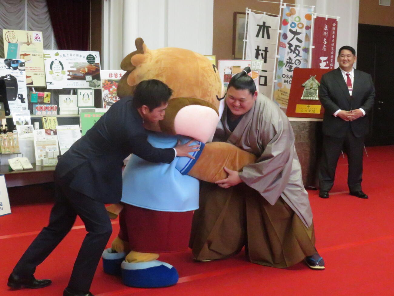 大の里（右）は要請を受け、大阪府の公式キャラクター、もずやん（中央）と相撲を取っていると、大阪府の吉村知事が加勢してきた。右後方は阿武松親方
