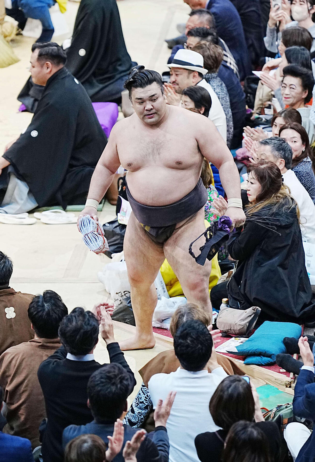1敗を守った霧島は懸賞の束を手に花道を引き揚げる。後方左は審判を務める師匠の音羽山親方（撮影・小沢裕）