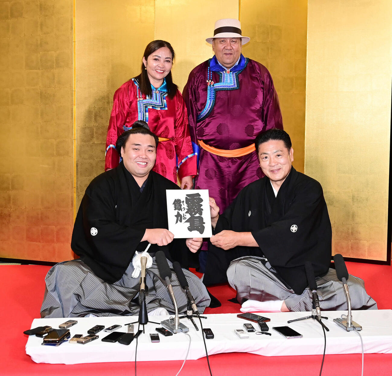 大関昇進伝達式を終えた霧馬山（前列左）は陸奥親方から授かった現役時代のしこ名「霧島」と記された色紙を手に笑顔。後列左は母エンフゲレルさん、同右は父ビャンブチュルンさん（2023年5月31日撮影）