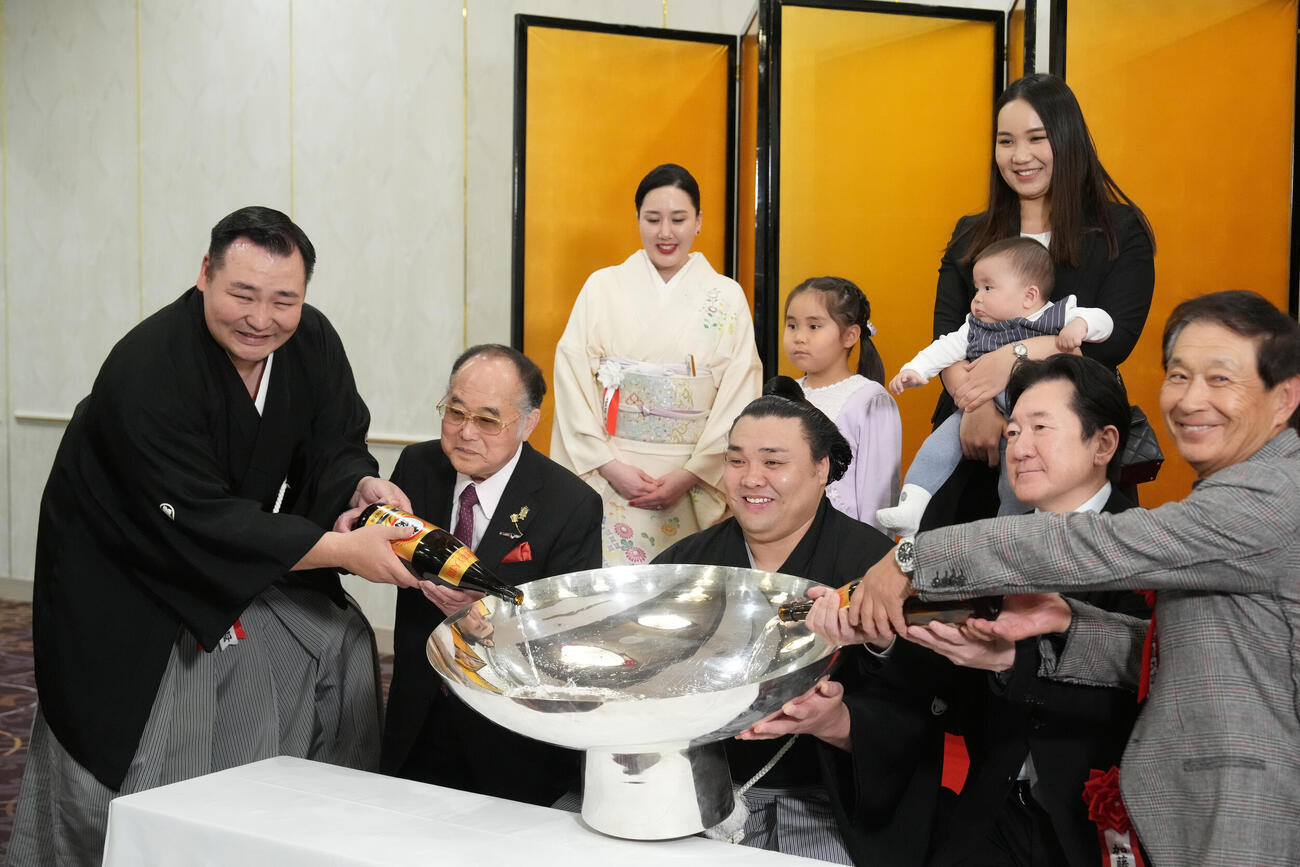 千秋楽パーティー会場で師匠の音羽山親方（左）や後援会関係者から銀杯にお祝いの酒をそそがれ笑顔を見せる霧島（中央）。後方左から音羽山夫人、霧島の長女アヤゴーちゃん、長男トゥグドゥルくんを抱くホラン夫人＝2026年3月22日