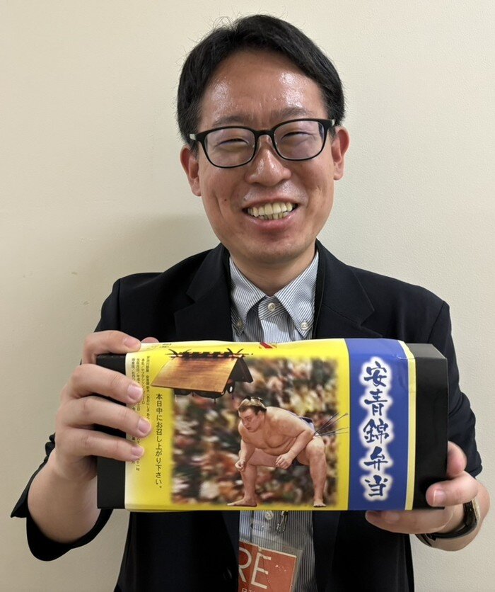 夏場所初日に販売された安青錦弁当を持つ本紙記者