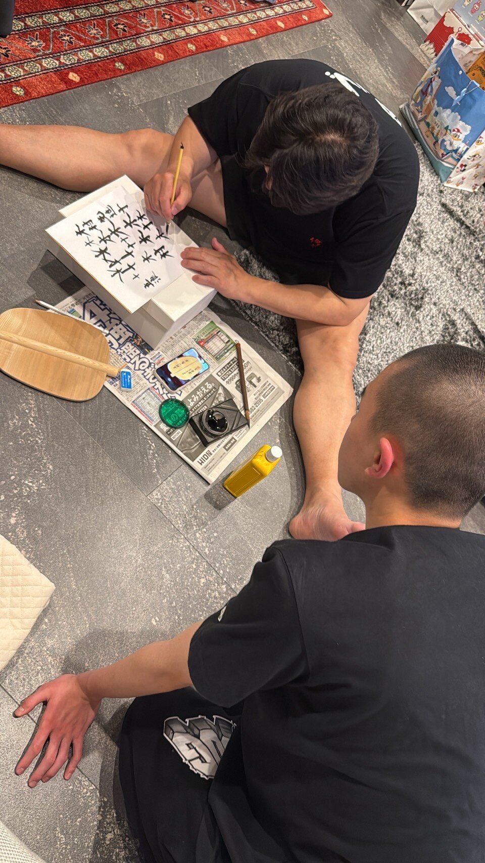 軍配に書き入れる文字を練習する立浪親方（上）と見つめる木村先進（立浪部屋提供）