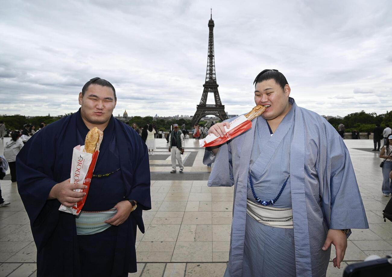 大相撲パリ公演を前に、エッフェル塔の前でフランスパンを食べる大の里（右）と豊昇龍の両横綱（共同）