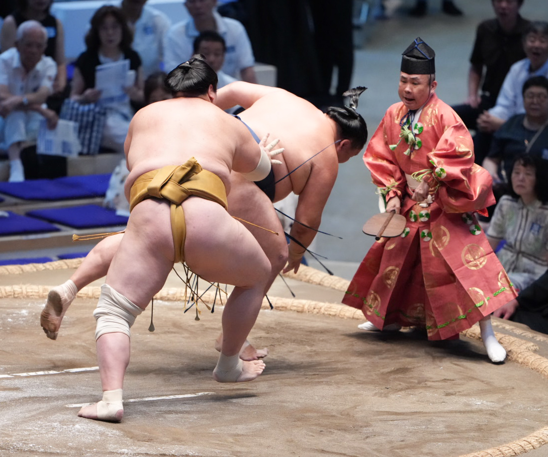 輝（手前）にいなされた玉鷲は取組を裁いていた行司の木村勘九郎（右）の方へ追いやられる（撮影・小沢裕）