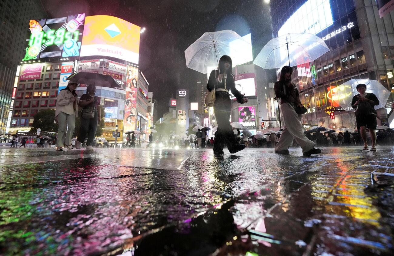 雨が降る中、東京・渋谷のスクランブル交差点を行き交う人たち＝20日夜（共同）