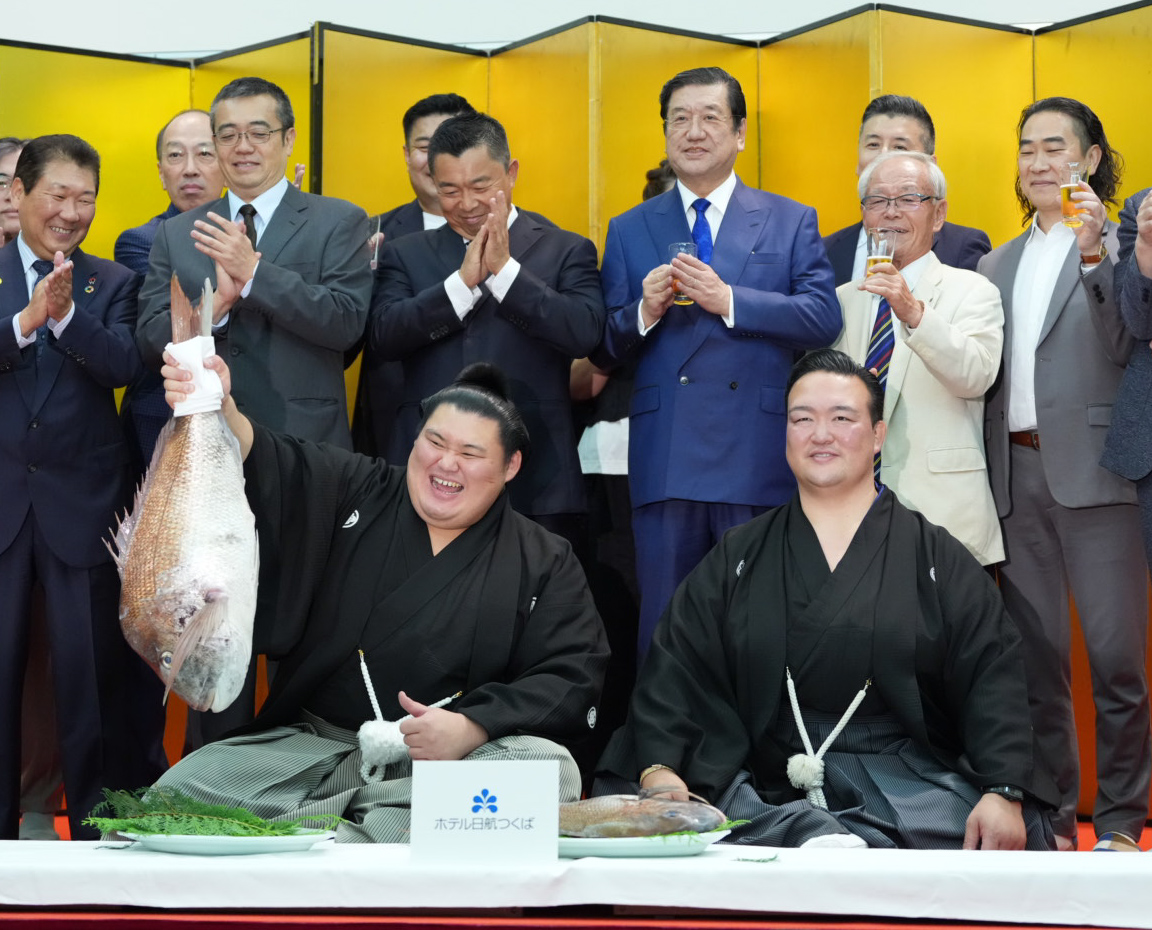 千秋楽パーティーで関係者の祝福を受けながらお祝いのタイを両手で持ち上げる大の里。右は師匠の二所ノ関親方（撮影・小沢裕）