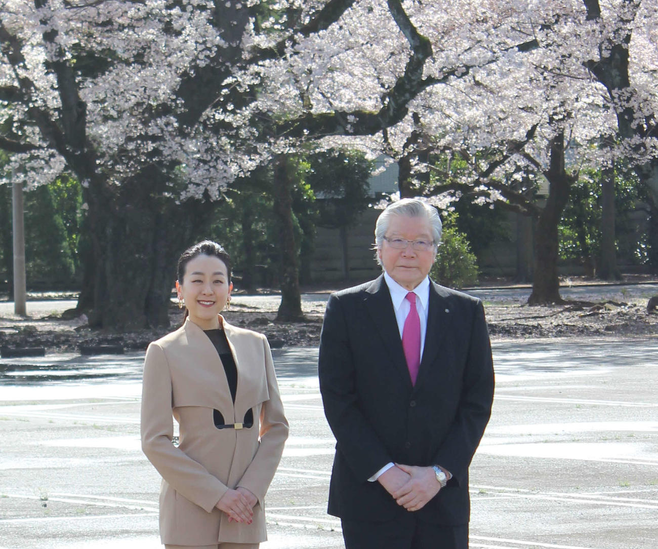 満開の桜をバックに建設予定地に立つ浅田さんと村山社長