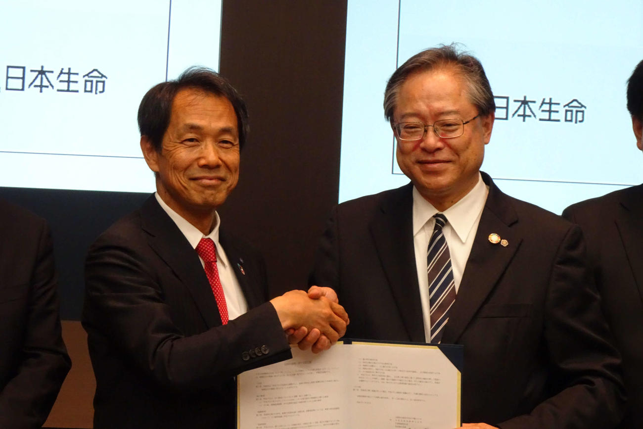 締結書を手に握手する日本生命清水博社長と城南信用金庫川本恭治理事長（右）