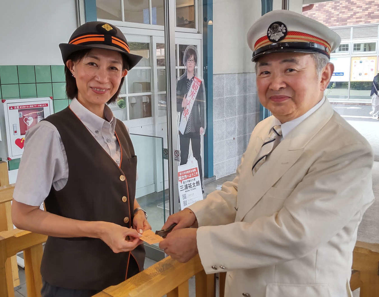 切符へのはさみ入れを行う沼本忠次さん（右）と国立駅の岡崎やよい駅長