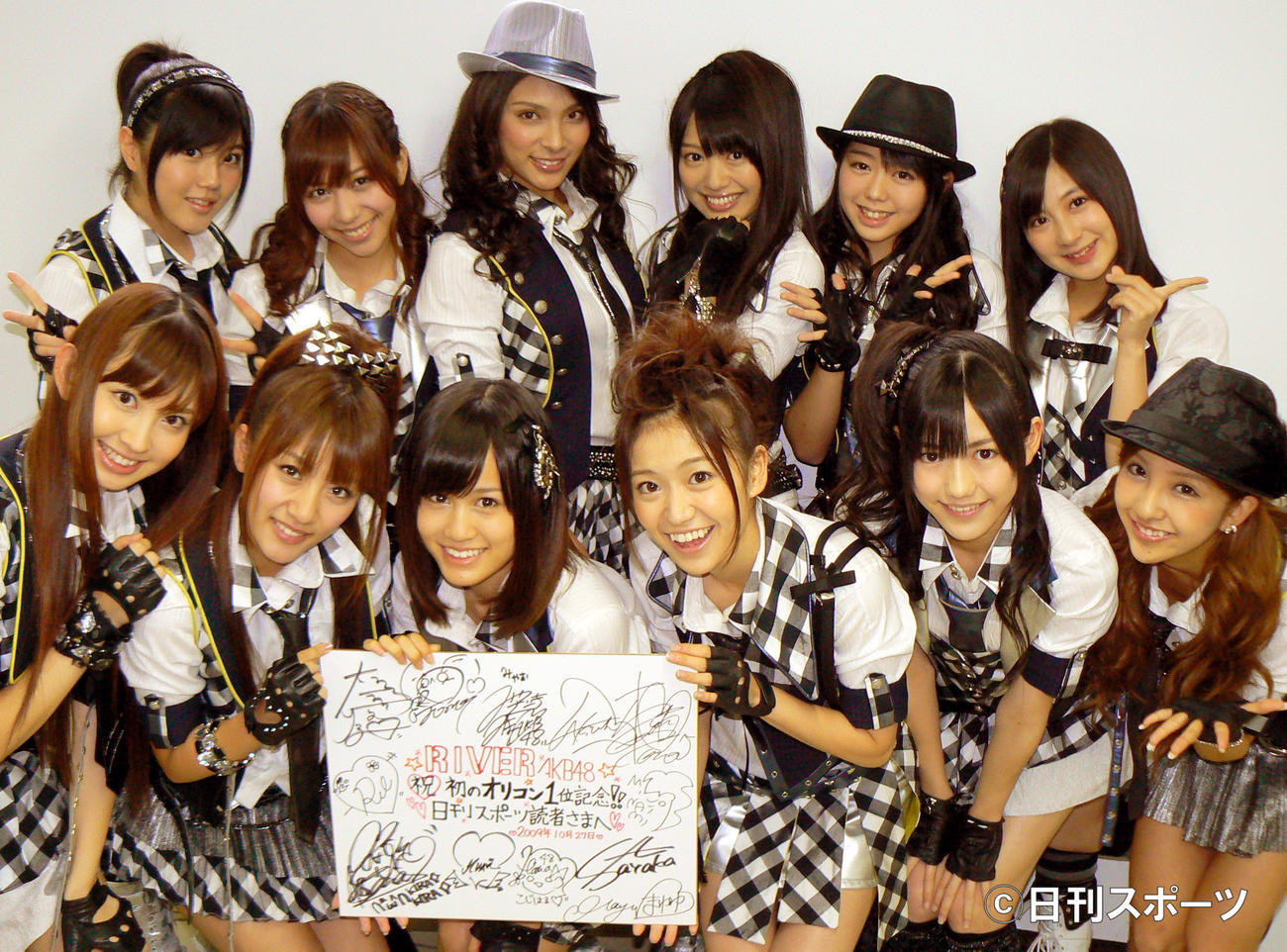 初のチャート1位を記念して、サイン色紙をプレゼントするAKB48。後列左から6人目が峯岸みなみ＝09年10月