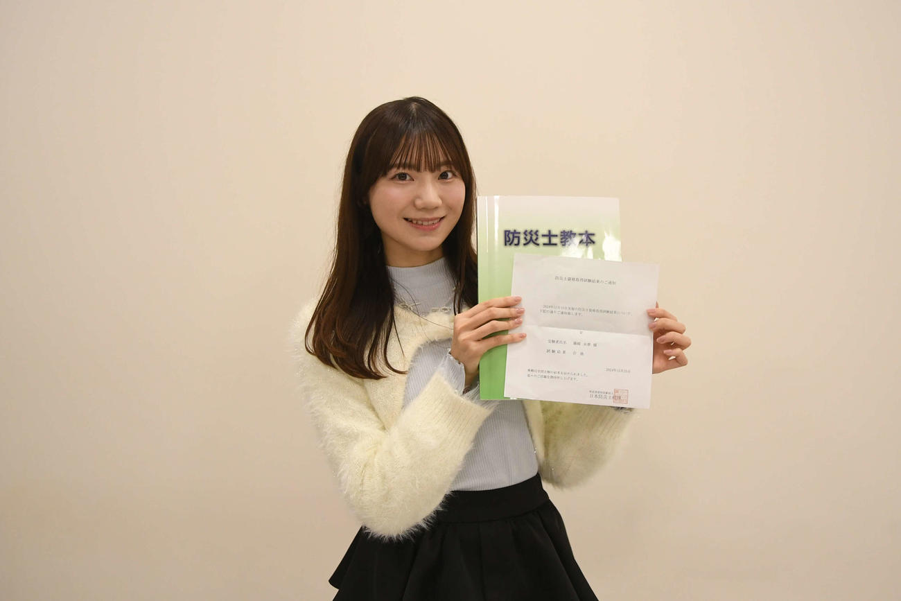 防災士資格試験の合格通知書と教本を手にするNGT48藤崎未夢
