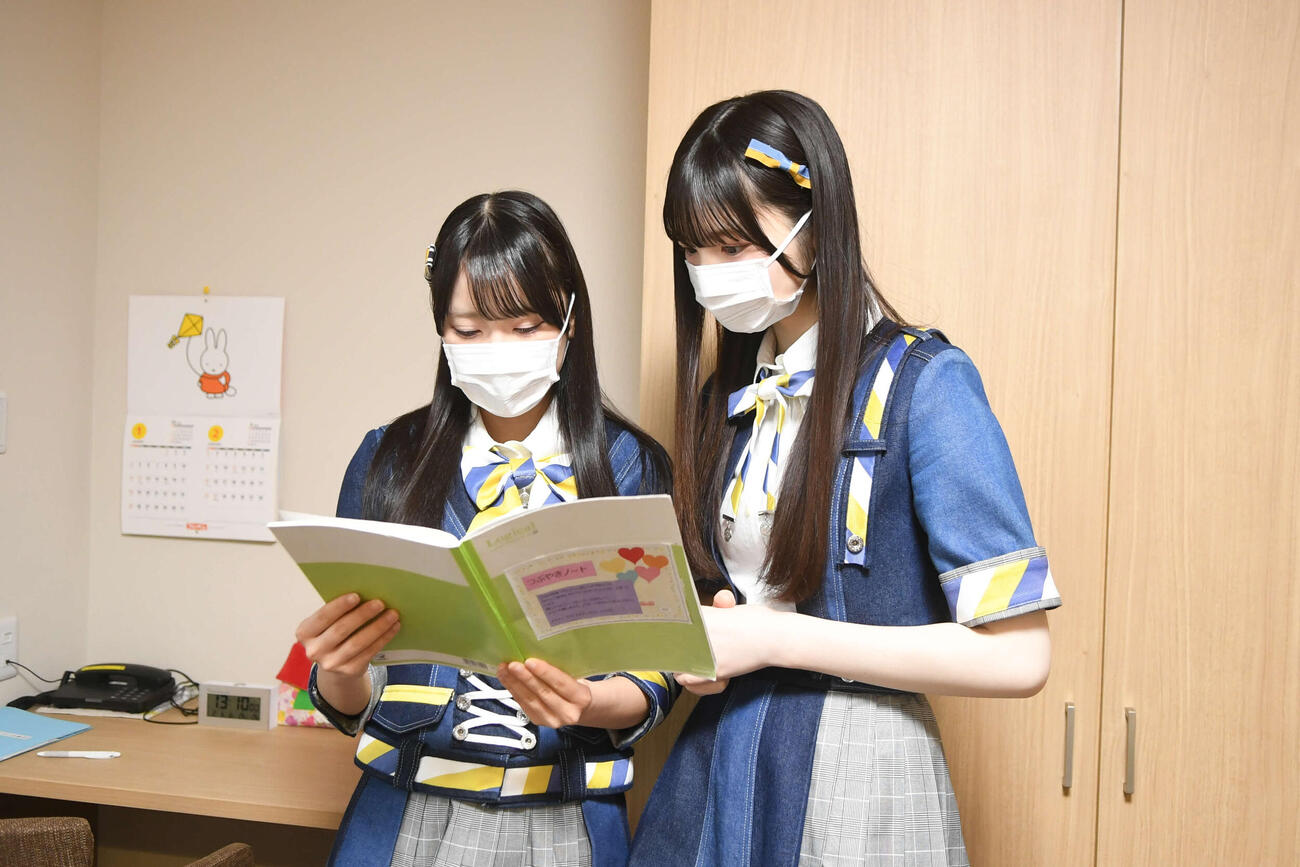 ハウス内を見学し、利用者が書きつなぐノートを読むAKB48丸山ひなた（左）と大賀彩姫