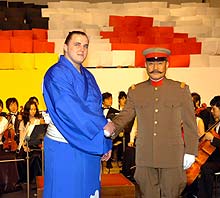 試写会でドイツと日本の国旗の人文字をバックに握手する松平健（右）と把瑠都