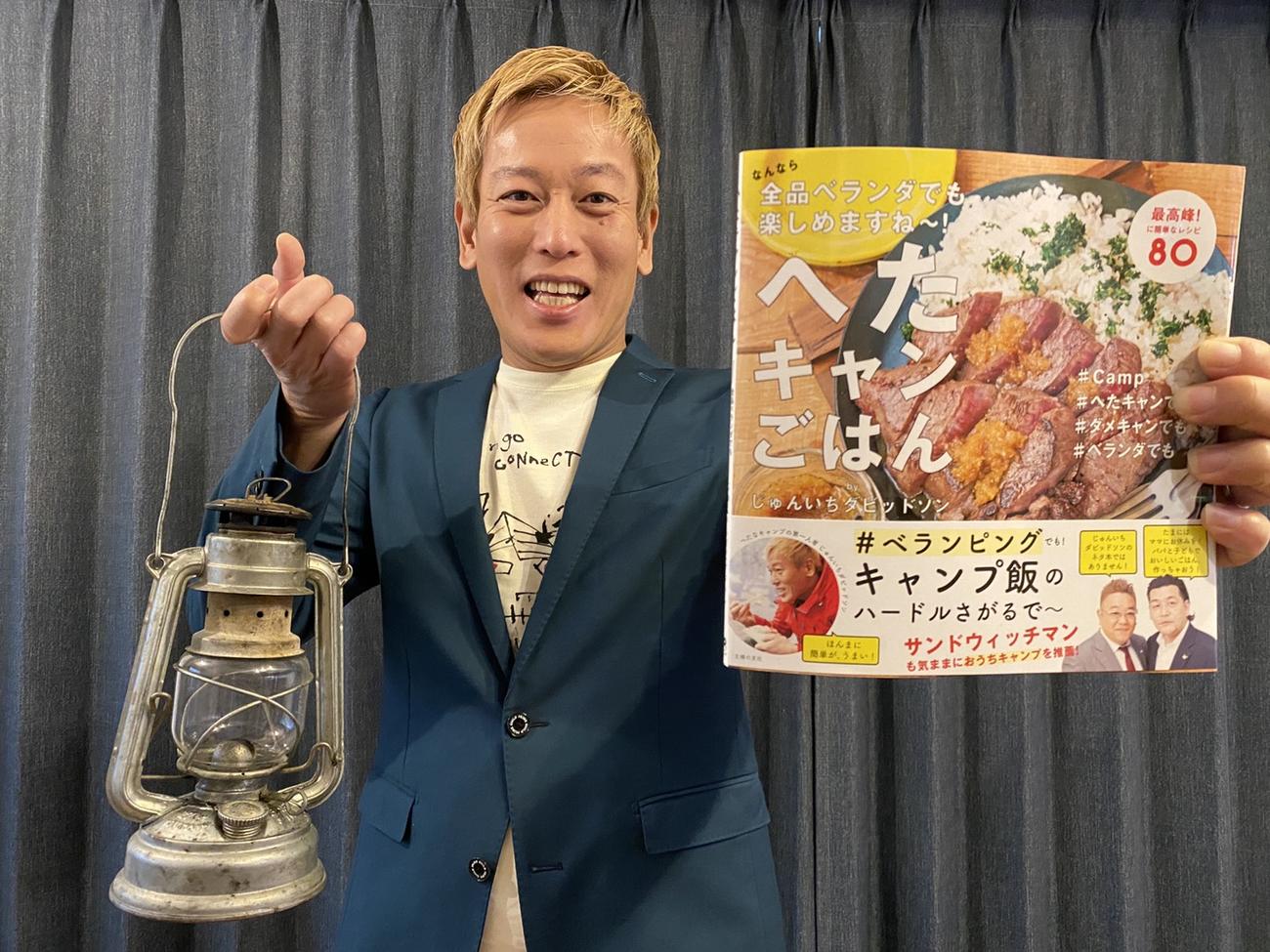 著書「へたキャンごはん　なんなら全品ベランダでも楽しめますね～！」を手にする、じゅんいちダビッドソン