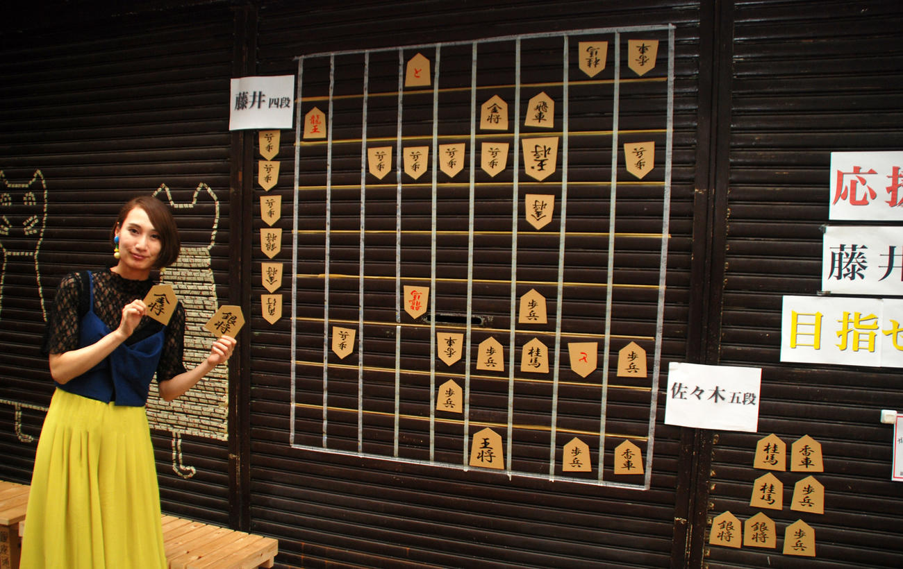 愛知県瀬戸市の「せと銀座通り商店街」の空き店舗のシャッターに張り付けられるジャンボ将棋盤、手作りの駒を持つ飯島加奈さん（撮影・松浦隆司）