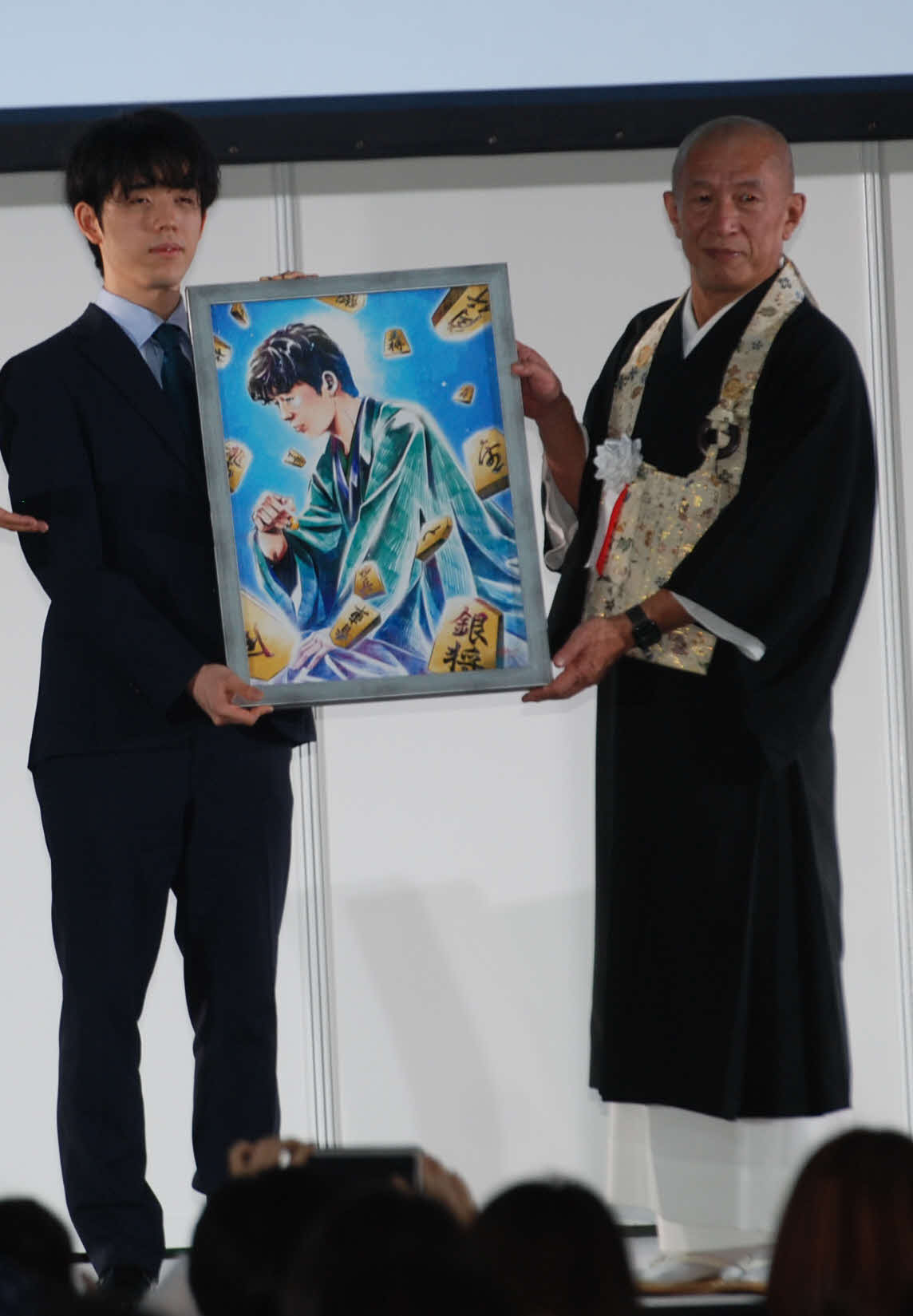 名古屋市内で行われた「棋聖戦防衛祝賀会」でポスターに使われた似顔絵を贈られた藤井聡太2冠（左）（撮影・松浦隆司）
