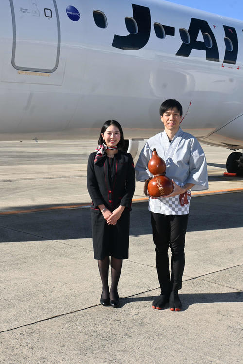 服部天神宮の「ご神水」を航空会社「ジェイエア」の客室乗務員に渡す「神主アドベンチャーランナー」の北田雄夫さん（撮影・松浦隆司）