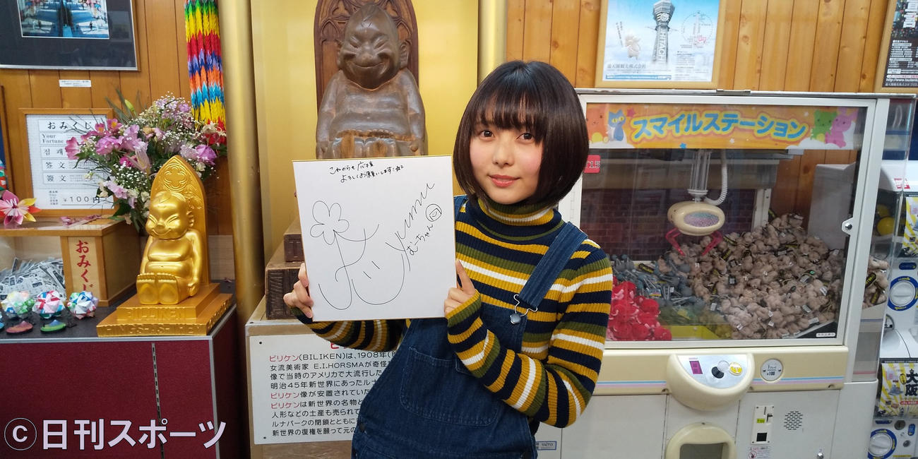 ビリケンさんを背に山崎歩夢がサイン入り色紙を持って撮影