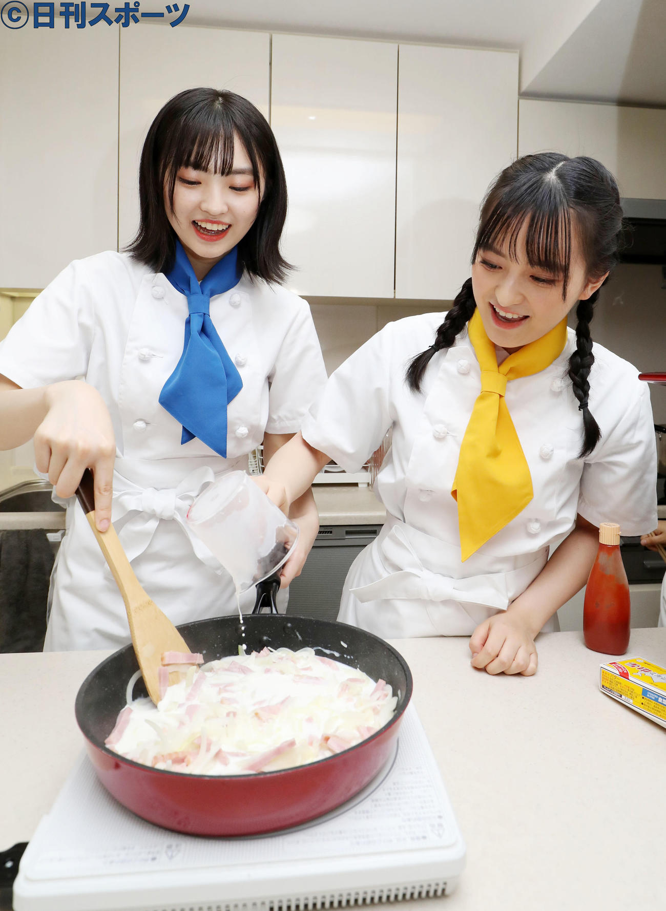 タマネギとベーコンのフライパンに牛乳を加える清井、左は炒める春名