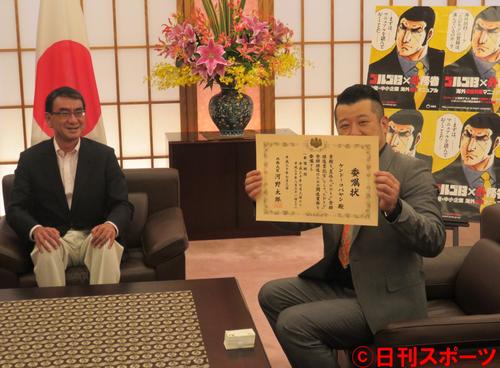 河野太郎外務大臣(左)から渡された、「夏休み『たびレジ』登録推進書記官」委嘱状を手にするケンドーコバヤシ