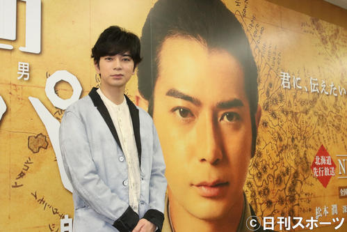 作品の巨大パネルを背にする松本（撮影・西塚祐司）