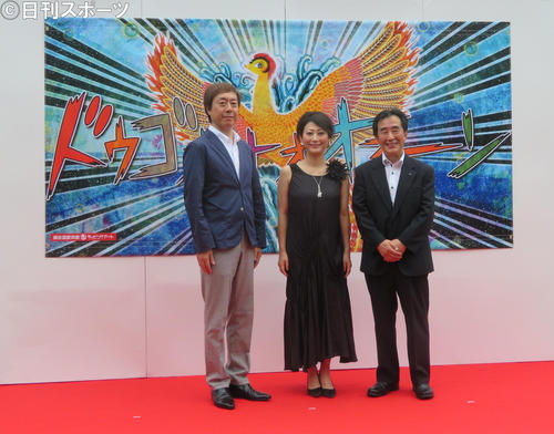 道後温泉本館ラッピングアートのウォールアートパネルの前に立つ友近（中央）。左はポニーキャニオン経営戦略本部の石川和雄副本部長、右は松山市の梅岡伸一郎副市長