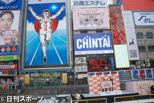 大阪・道頓堀名物のネオン広告塔「グリコのランナー」の横に設置された「道頓堀改源ビジョン」に登場した改源錠限定パッケージに起用された「なごむくん」、右下はスピードワゴン（撮影・松浦隆司）