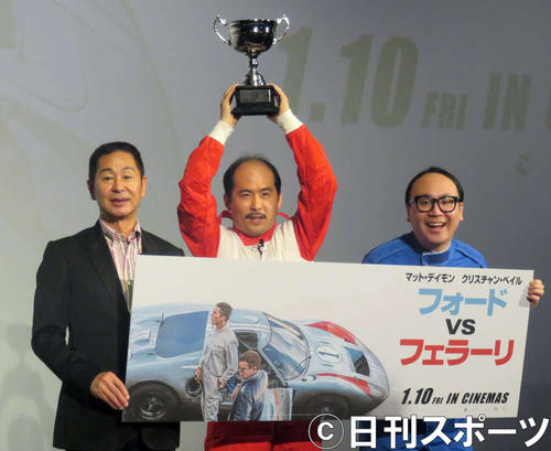 伝説のレーサー、ドリキンこと土屋圭一氏（左）にレーシングゲームで勝ってトロフィーを掲げるトレンディエンジェル斎藤司（中央）とたかし