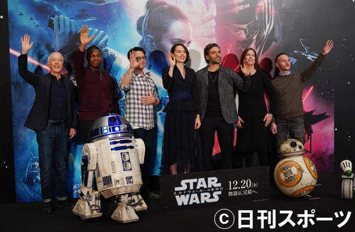 映画「スター・ウォーズ／スカイウォーカーの夜明け」のキャストらの来日記者会見でカメラに向かって手を振る、左からアンソニー・ダニエルズ、ジョン・ボイエガ、J．J．エイブラムス監督、デイジー・リドリー、オスカー・アイザック、プロデューサーのミシェル・レイワン氏、脚本のクリス・テリオ氏（2019年12月12日撮影）